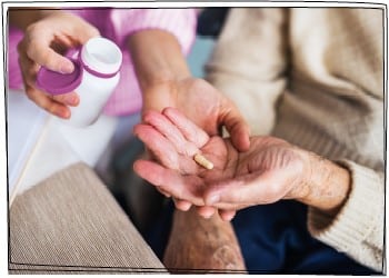 Eine Pflegefachkraft überreicht einer älteren Dame eine Tablette in ihre linke Hand.