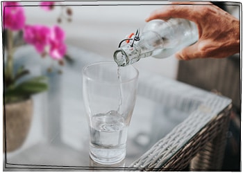 Aus einer Glasflasche wird Wasser in ein Glas gefüllt.