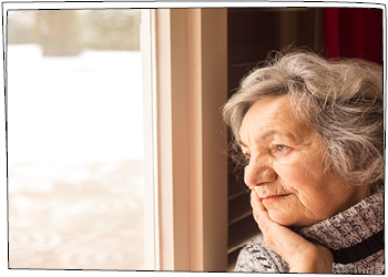 Altersdepression: Bedrückt wirkende ältere Dame sieht mit leerem Blick aus einem Fenster.