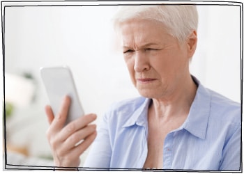 Alterssichtigkeit: Eine ältere Dame schaut mit zusammen gekniffenen Augen auf ihr Handy.
