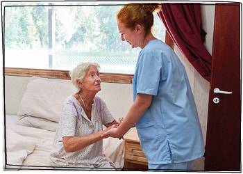 Eine Pflegefachkraft hält die Hände einer Senioren, um sie zu mobilisieren und ihr beim Aufstehen aus dem Bett zu helfen.