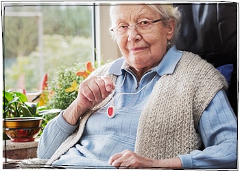 Eine Seniorin mit einem Hausnotrufknopf, den sie wie eine Kette um ihren Hals trägt.