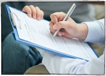 Pflegedokumentation: Eine männliche Person füllt mit einer Person im Hintergrund einen Anamnesebogen aus.