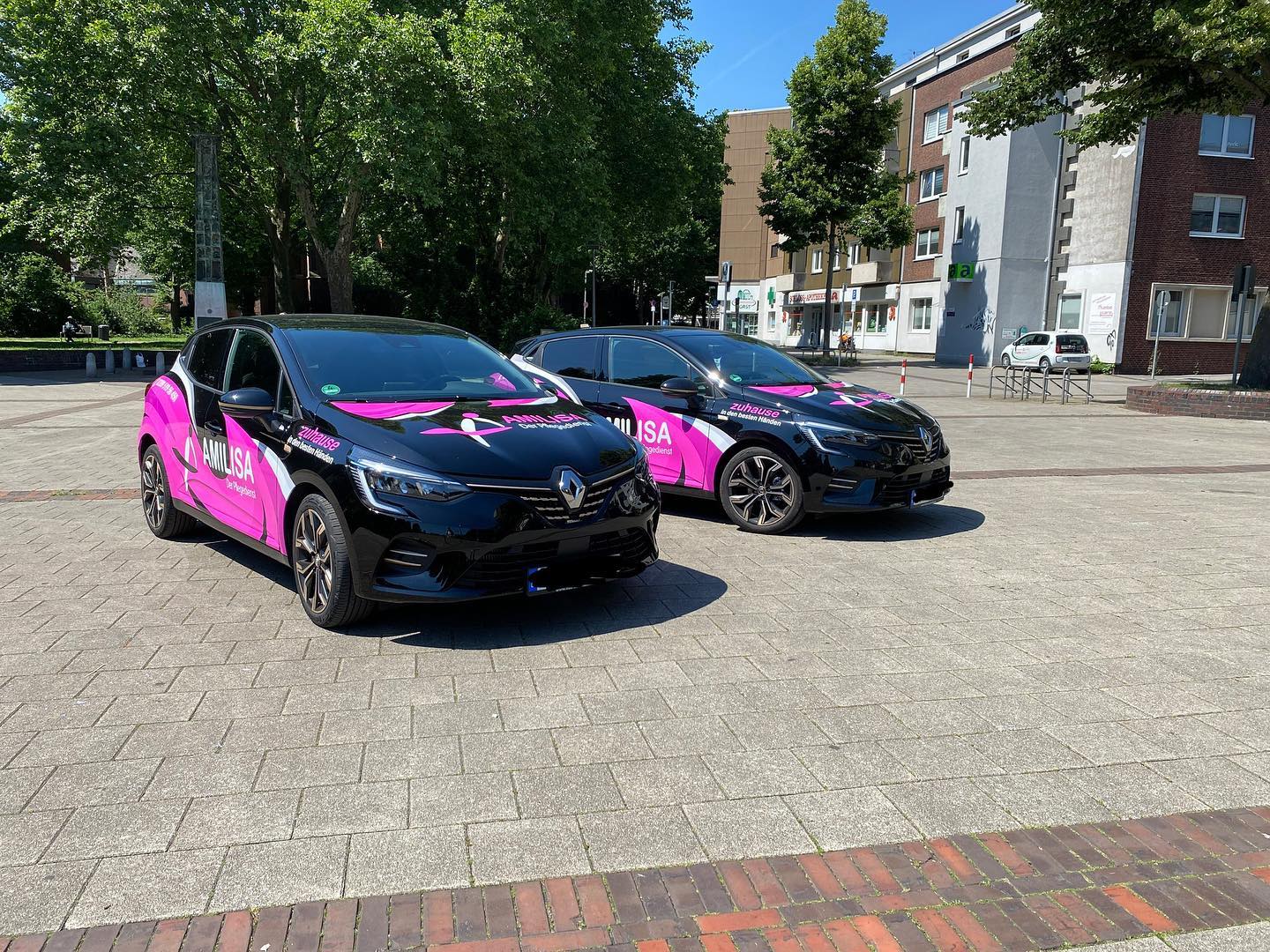 Zwei Fahrzeuge von Amilisa mit pinkfarbener Beschriftung stehen nebeneinander auf einem Platz in Gelsenkirchen